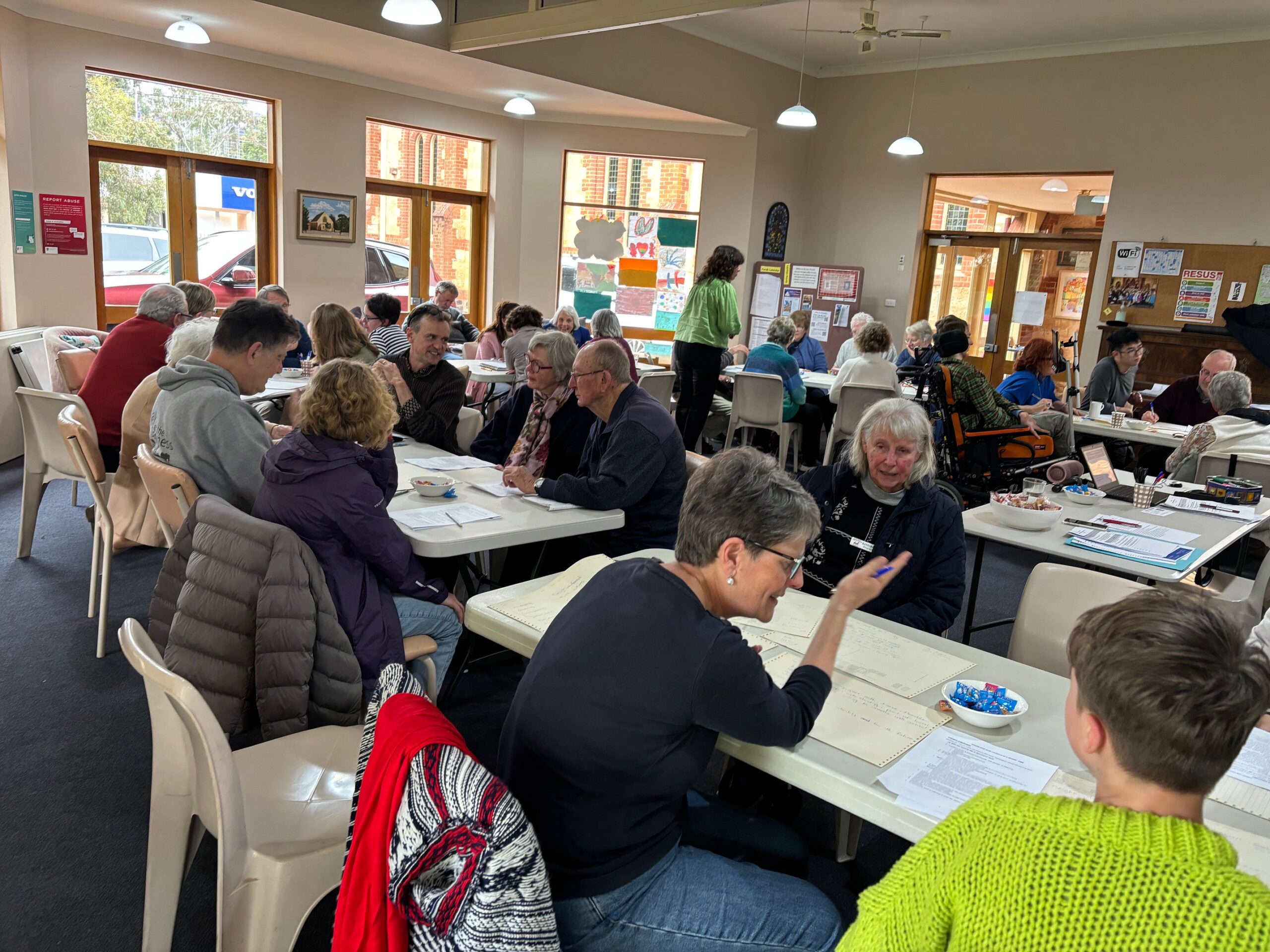 people sitting at trestle tables indoors, discussing wiht each other