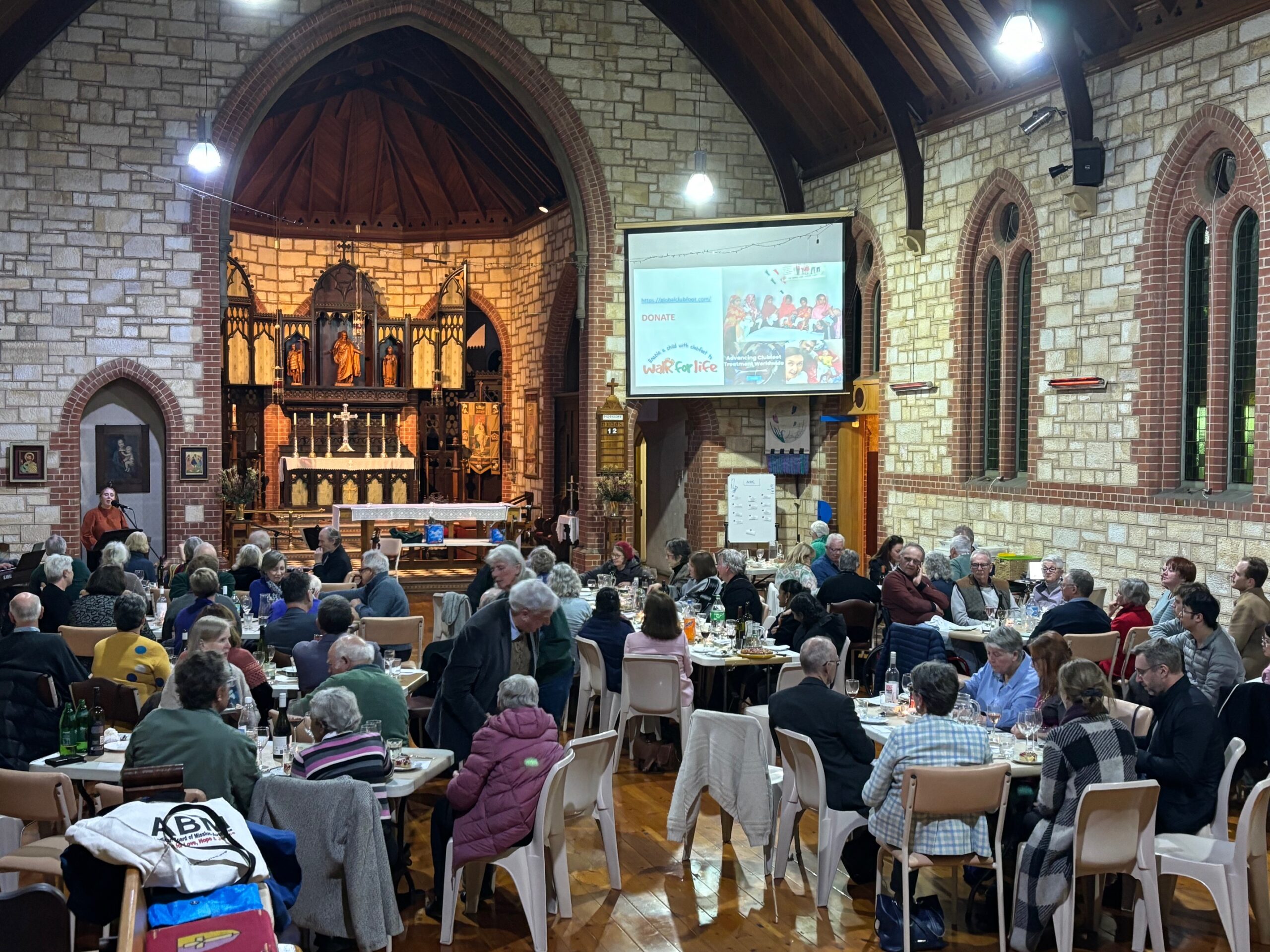 group of people sitting at tables in a church, eating food and listening to a speaker