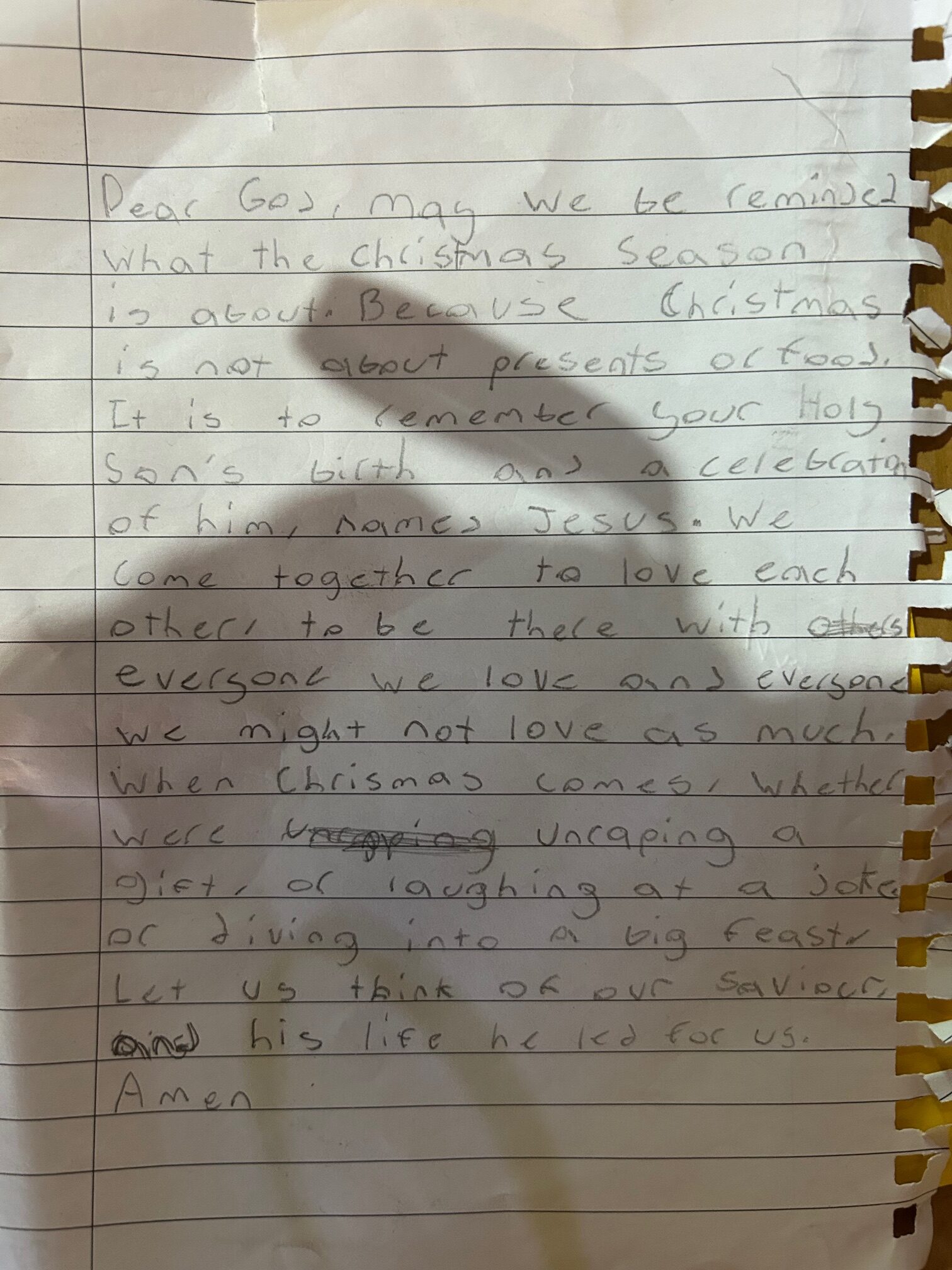 Lined piece of paper with the following handwriting: Dear God, may we be reminded what the Christmas Season is about. Because Christmas is not about presents or food. It is to remember your Hold Son's birth and a celebration of him, named Jesus. We come together to love each other, to be there with everyone we love and everyone we might not love as much. When Chismas comes, whether we're unraping a gift, or laughing at a joke, or diving into a big feast, let us think of our saviour, and his life he led for us. Amen