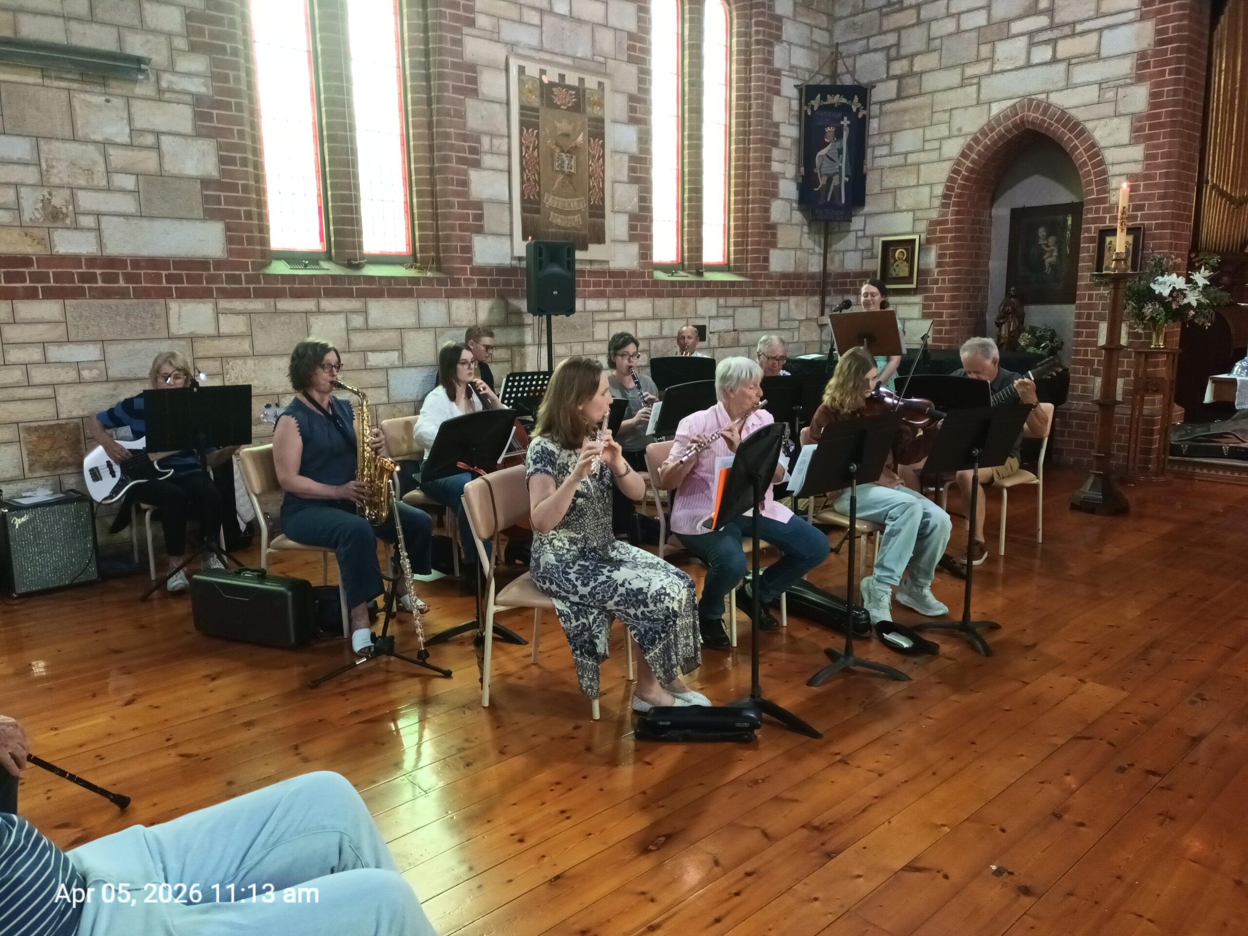 A dozen musicians singing and playing instruments in a church.