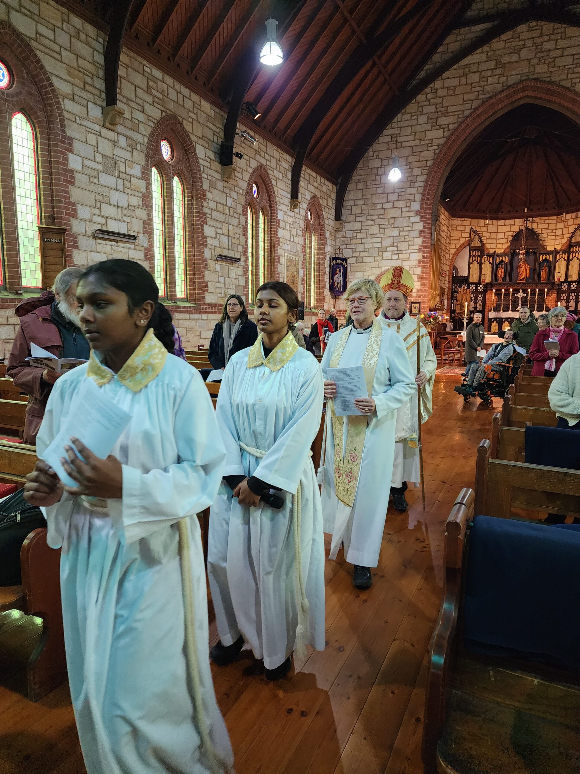 Procession of people in robes walking through the aisle of a church.