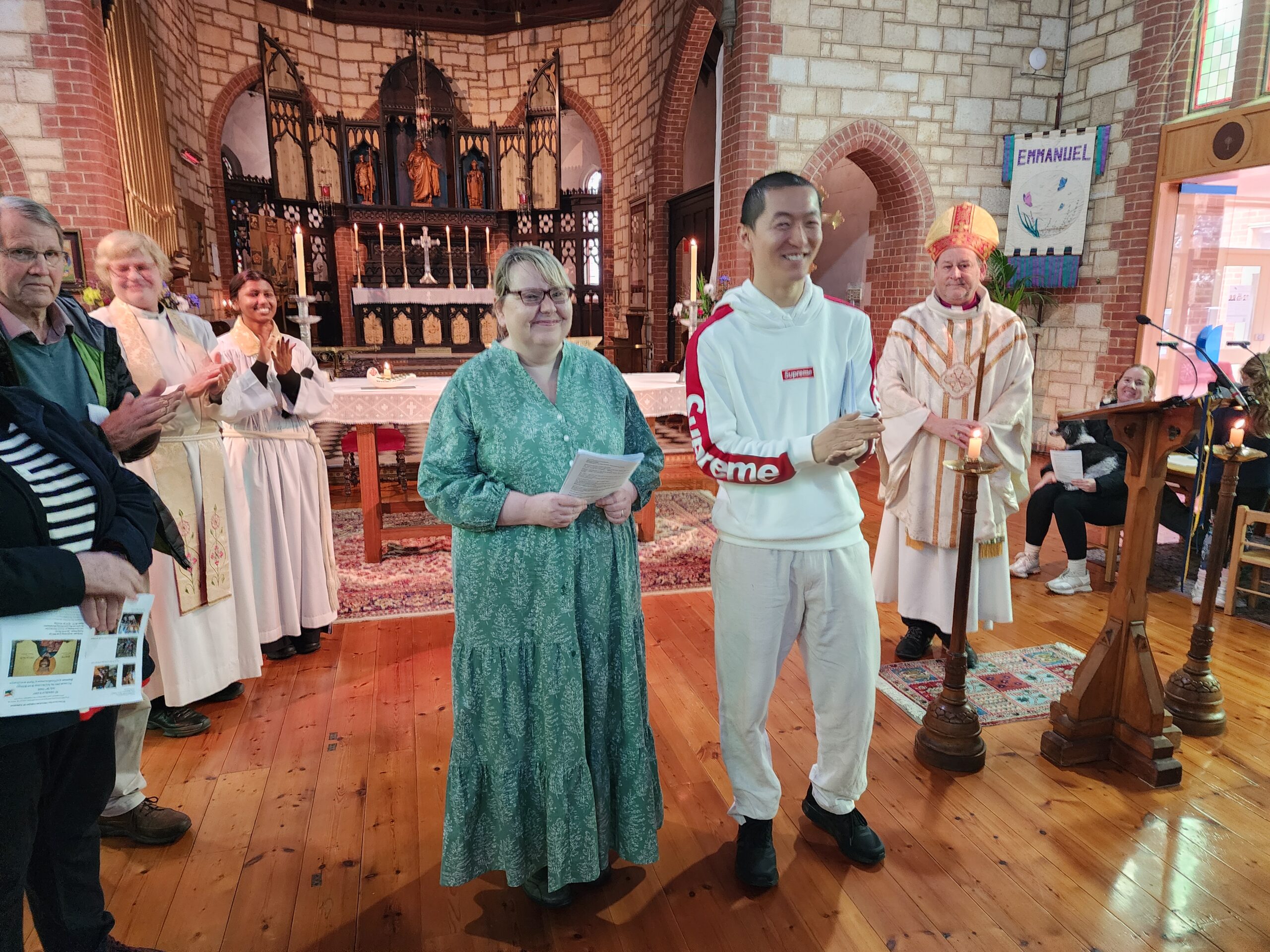 Two people standing smiling in front of a church altar surrounded by clapping people.