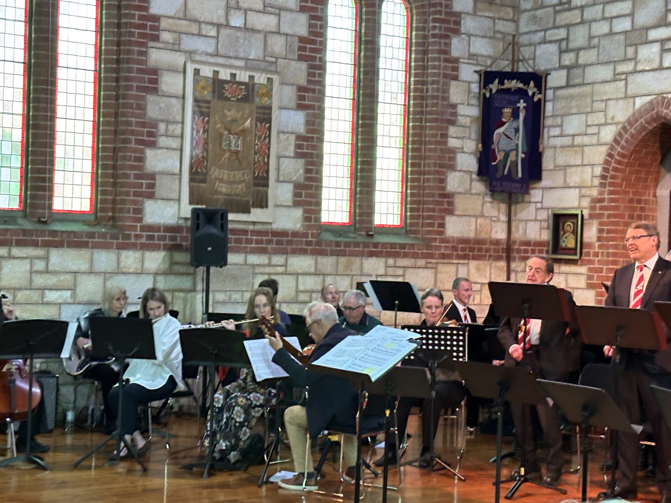 Group of musicians playing instruments in the corner of a church, with choristers singing in front of them.