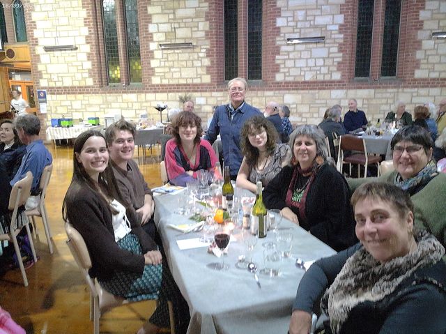 Group of smiling people sitting around a dining table with glasses and wine bottles in a church.