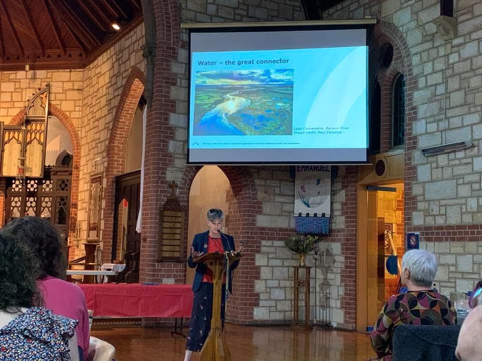 Person standing at a lectern talking below a slideshow screen in a church.